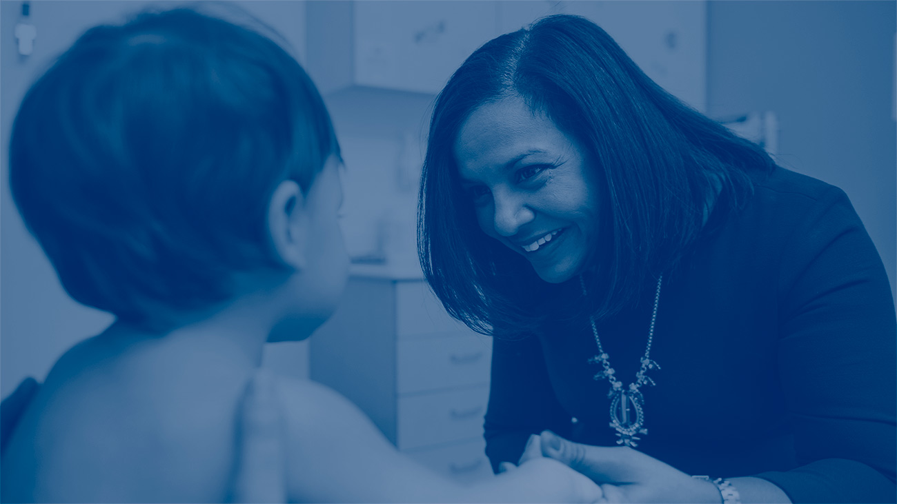 A woman with dark hair talks to a young toddler. The image has a dark blue tint laid over it so you can read the white words: Together, we're redefining healthcare in the Rocky Mountain region. The Pediatric Care Network with Children's Hospital Colorado helps improve lives with coordinated, quality care.